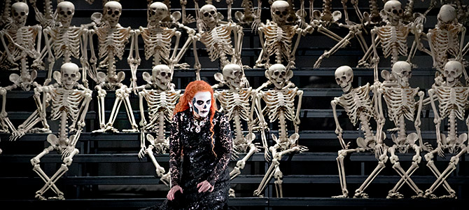 En sopran målad som en döskalle omgiven av många skelett i föreställningen La traviata av Verdi. 